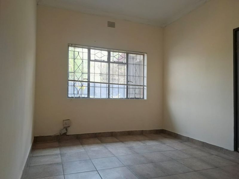 A vacant bedroom featuring tiled flooring, neutral walls, and a window fitted with security bars.