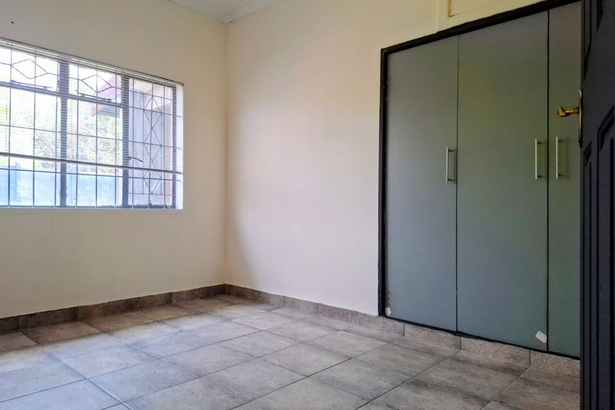 A vacant bedroom featuring tiled flooring, a built-in wardrobe, and a window fitted with security bars.