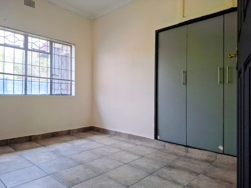 A vacant bedroom featuring tiled flooring, a built-in wardrobe, and a window fitted with security bars.