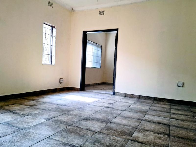 An empty living room featuring tiled flooring, security bars on the windows, and neutral wall finishes, offering a blank canvas for potential interior design.