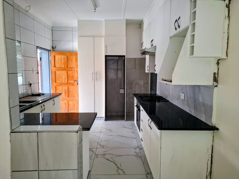 A functional kitchen featuring white cabinetry, black granite countertops, built-in oven, hob, and tiled flooring, offering a clean layout ready for final finishing touches.