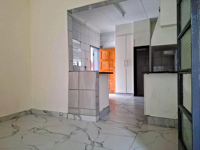 An empty kitchen featuring marble-look floor tiles, built-in cabinetry, a breakfast bar, and tiled splashbacks, offering a functional layout ready for personalization.