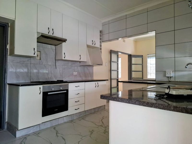 A functional kitchen featuring white cabinetry, granite countertops, built-in oven, gas hob, and tiled finishes, offering a clean and practical workspace.