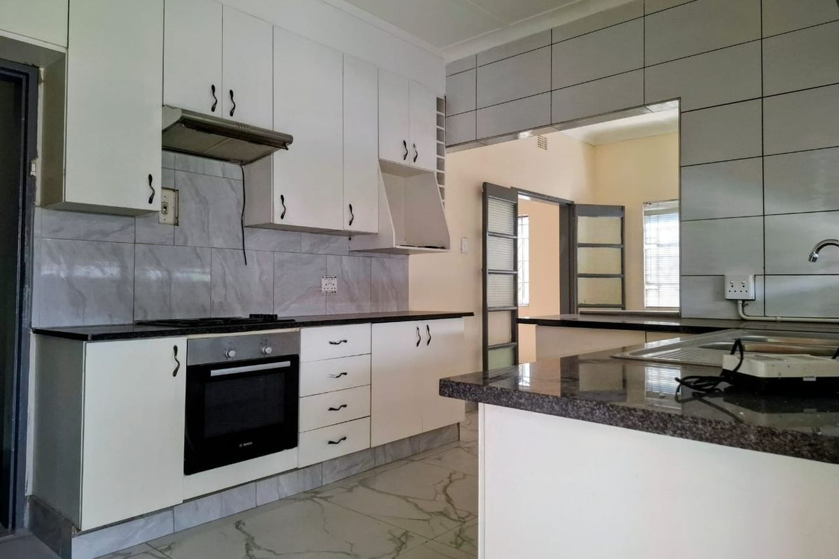 A functional kitchen featuring white cabinetry, granite countertops, built-in oven, gas hob, and tiled finishes, offering a clean and practical workspace.