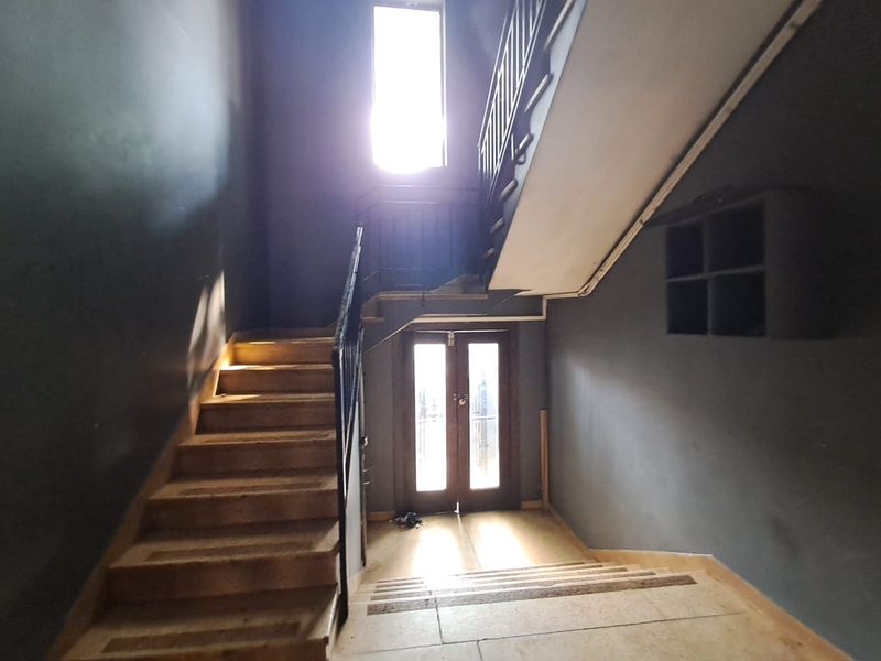 A spacious commercial hallway featuring a central staircase with metal handrails, double entrance doors, and built-in wall shelving.