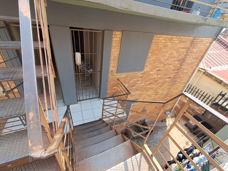 Exterior rear view of a commercial building featuring a metal staircase, security gate, and a utility sink area with brick facade finishes.
