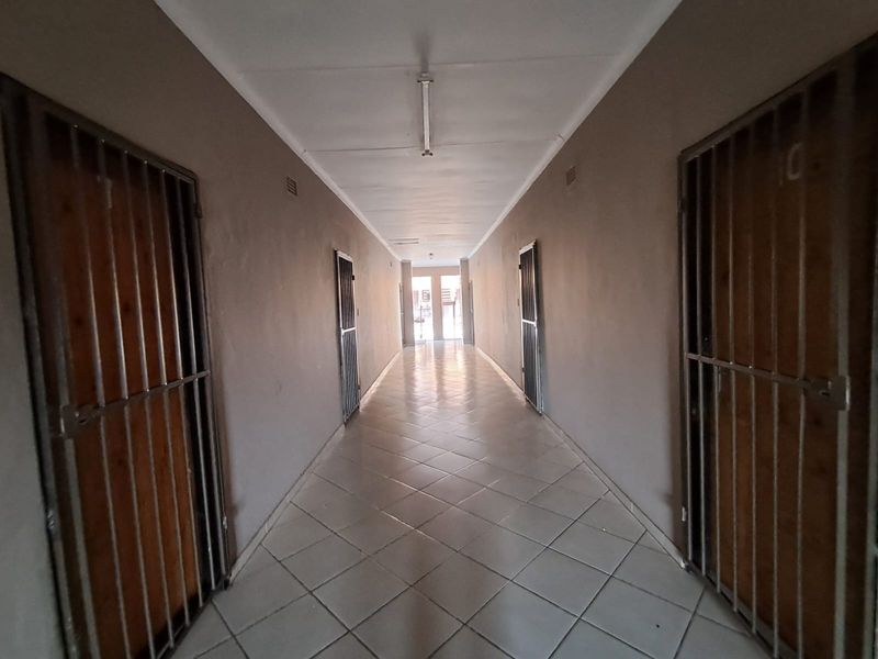 A long commercial hallway featuring tiled flooring, fluorescent lighting, and multiple security gates leading to individual units.