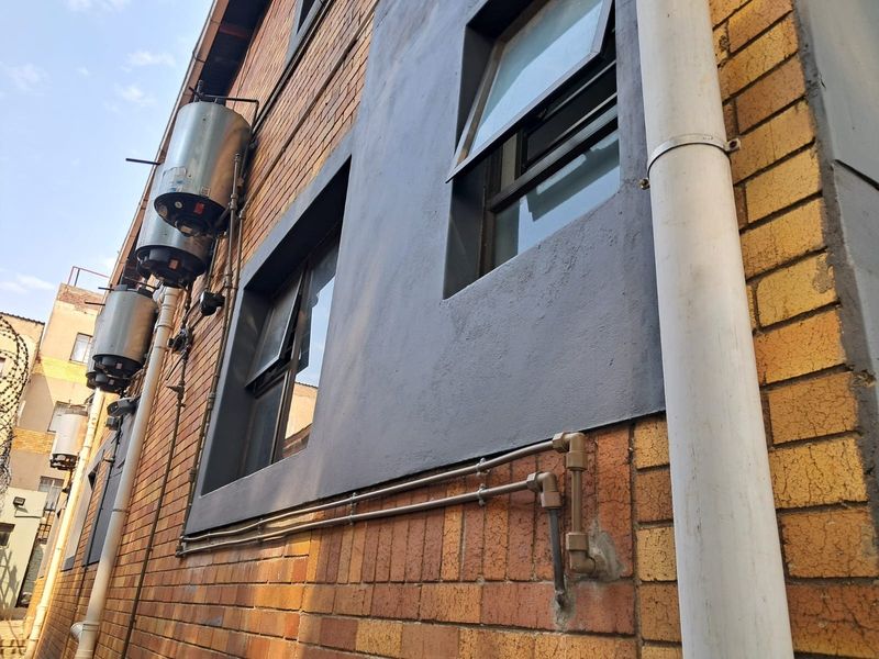 Exterior view of the building facade featuring exposed brickwork, external geysers, and functional casement windows with visible plumbing infrastructure.