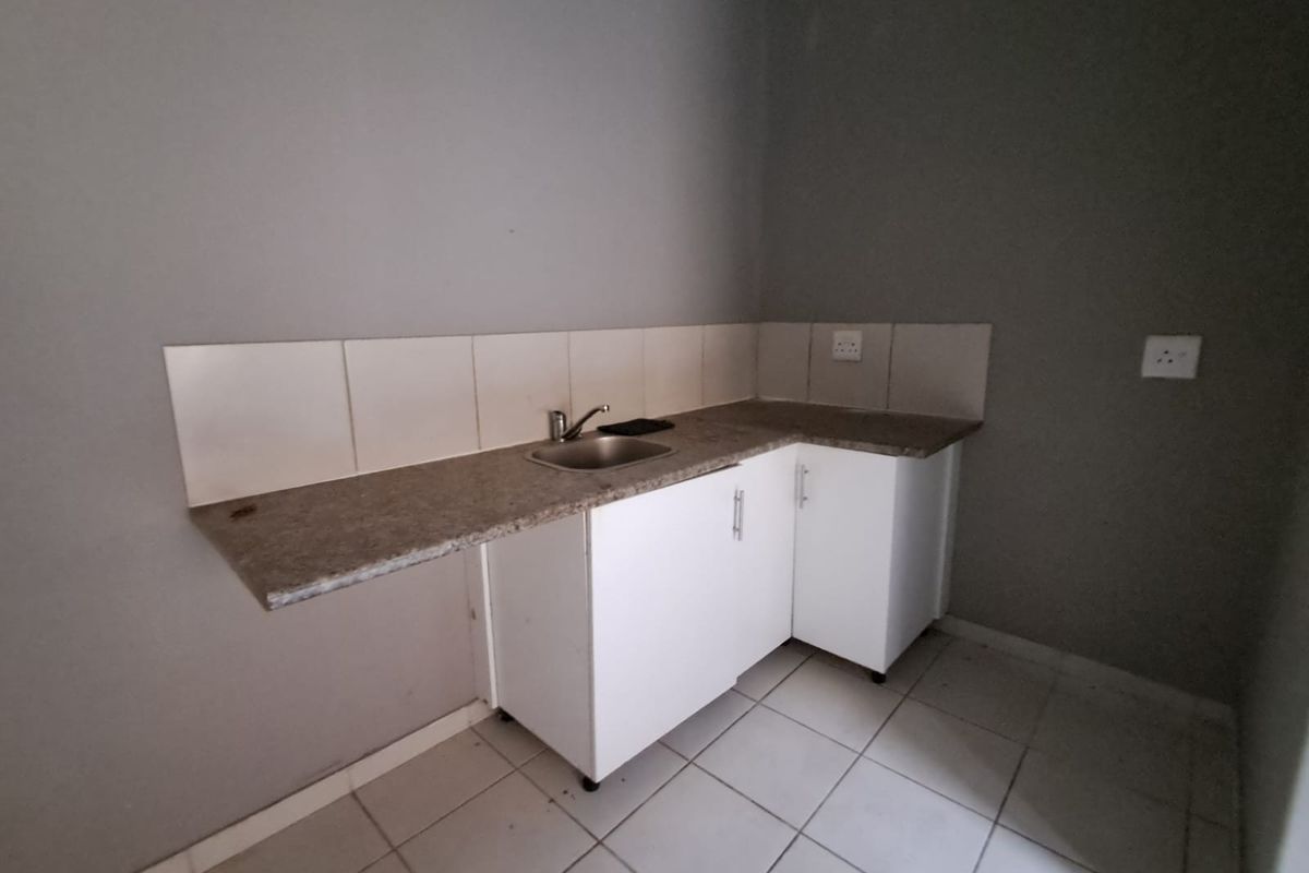 A compact, empty kitchen area featuring white built-in cabinetry, a laminate countertop with an integrated stainless steel sink, and tiled flooring.