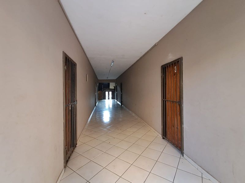 A long commercial hallway featuring tiled flooring, neutral walls, and security gates leading to individual units.