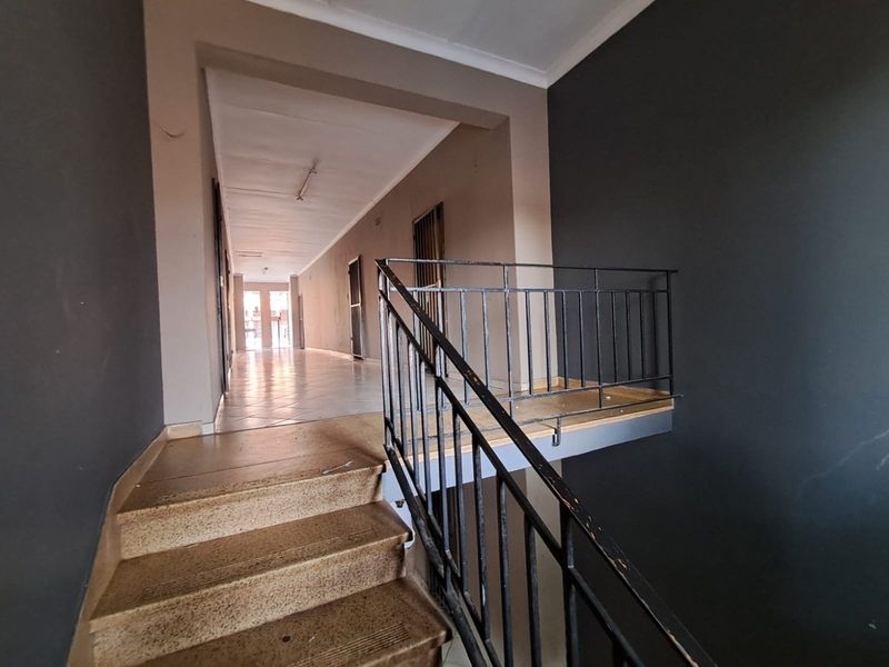 A commercial hallway featuring a staircase with a metal balustrade, tiled flooring, and neutral wall finishes, providing access to adjacent units.
