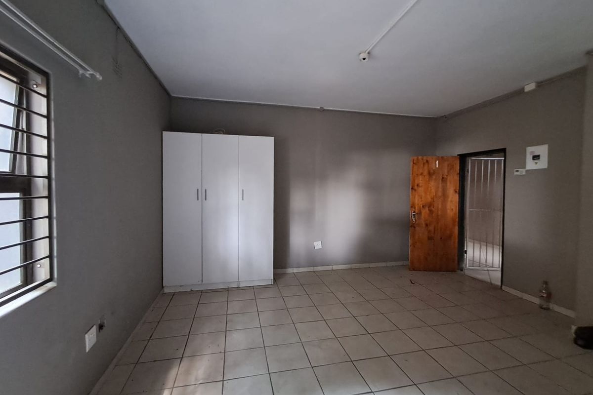 A functional bedroom space featuring tiled flooring, a built-in cupboard, and security features including burglar bars and a security gate.