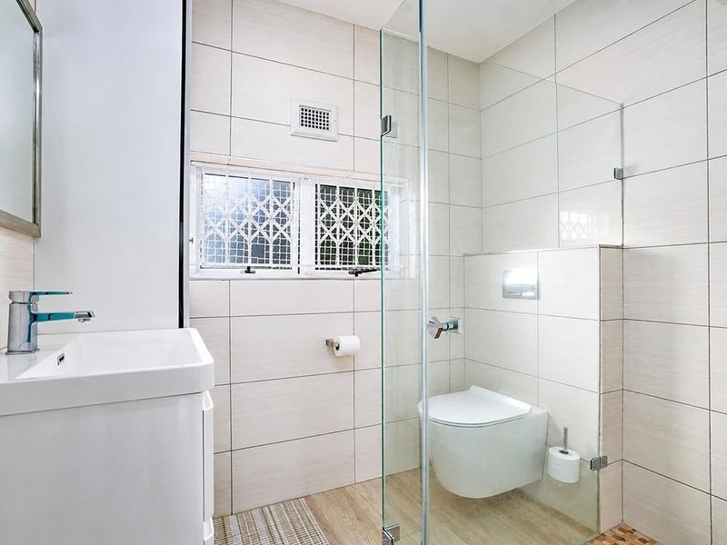 A modern, clean bathroom featuring a wall-mounted toilet, glass shower enclosure, and a vanity basin with contemporary chrome fixtures.