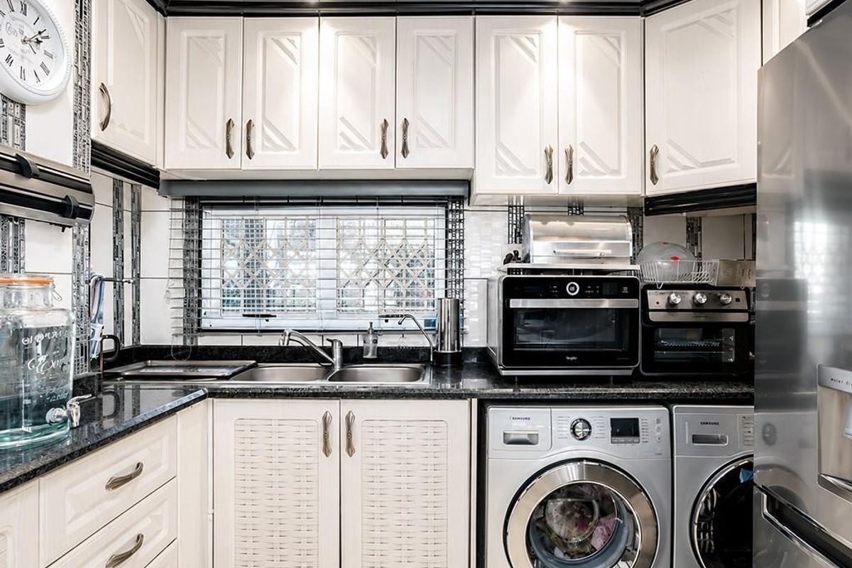A compact kitchen featuring white cabinetry, granite countertops, a double sink, and integrated laundry appliances, finished with a decorative tiled backsplash.