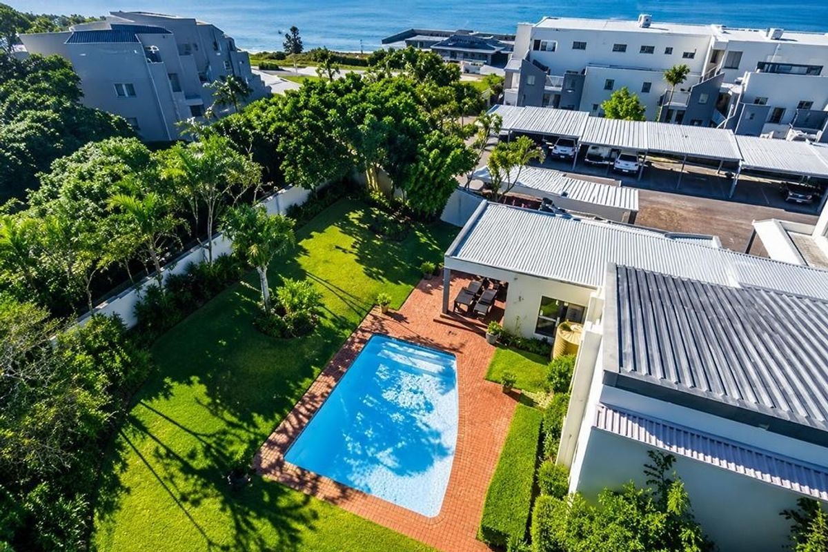 Aerial view of the apartment complex featuring a private swimming pool, covered patio, landscaped garden, and dedicated carport parking area.