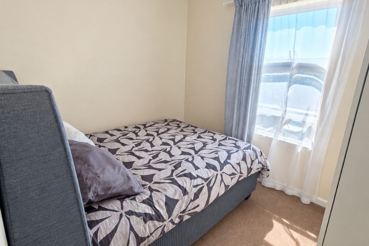 A compact bedroom featuring neutral wall tones, carpeted flooring, and a window with installed curtain rods.