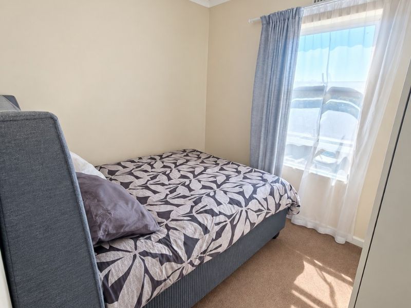 A compact bedroom featuring neutral wall tones, carpeted flooring, and a window with installed curtain rods.