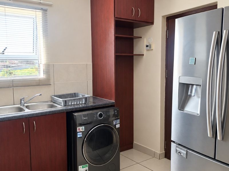 A functional laundry area featuring built-in dark wood cabinetry, a stainless steel double sink, tiled flooring, and space for laundry appliances.