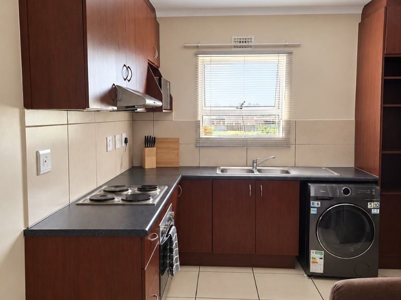 A functional kitchen featuring dark wood cabinetry, laminate countertops, a built-in electric hob, oven, and tiled flooring with a neutral backsplash.