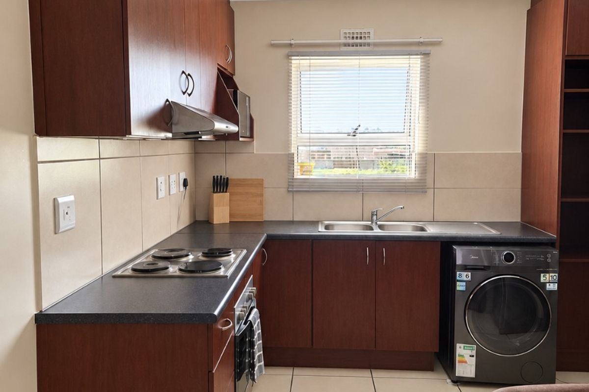 A functional kitchen featuring dark wood cabinetry, laminate countertops, a built-in electric hob, oven, and tiled flooring with a neutral backsplash.