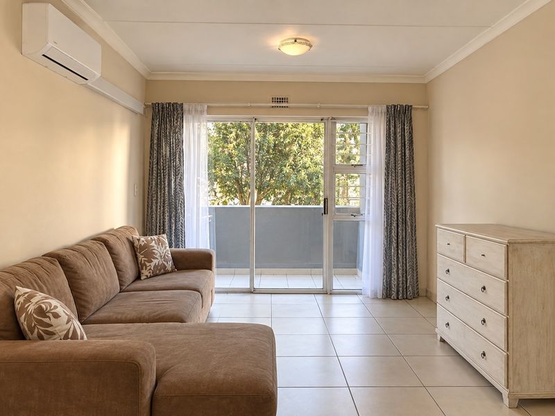 A bright living room featuring tiled flooring, a split-system air conditioner, and a sliding glass door providing access to a balcony.