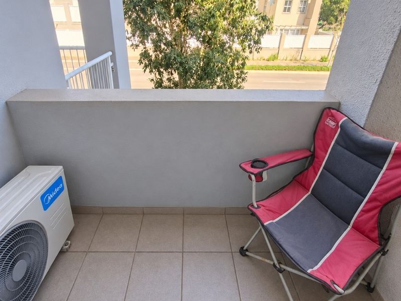 A compact apartment balcony featuring tiled flooring, a concrete balustrade, and an external air conditioning unit.