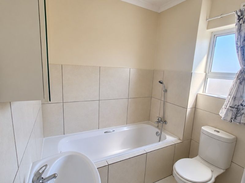 A functional bathroom featuring a bathtub with shower mixer, pedestal basin, and toilet, finished with neutral wall and floor tiles.
