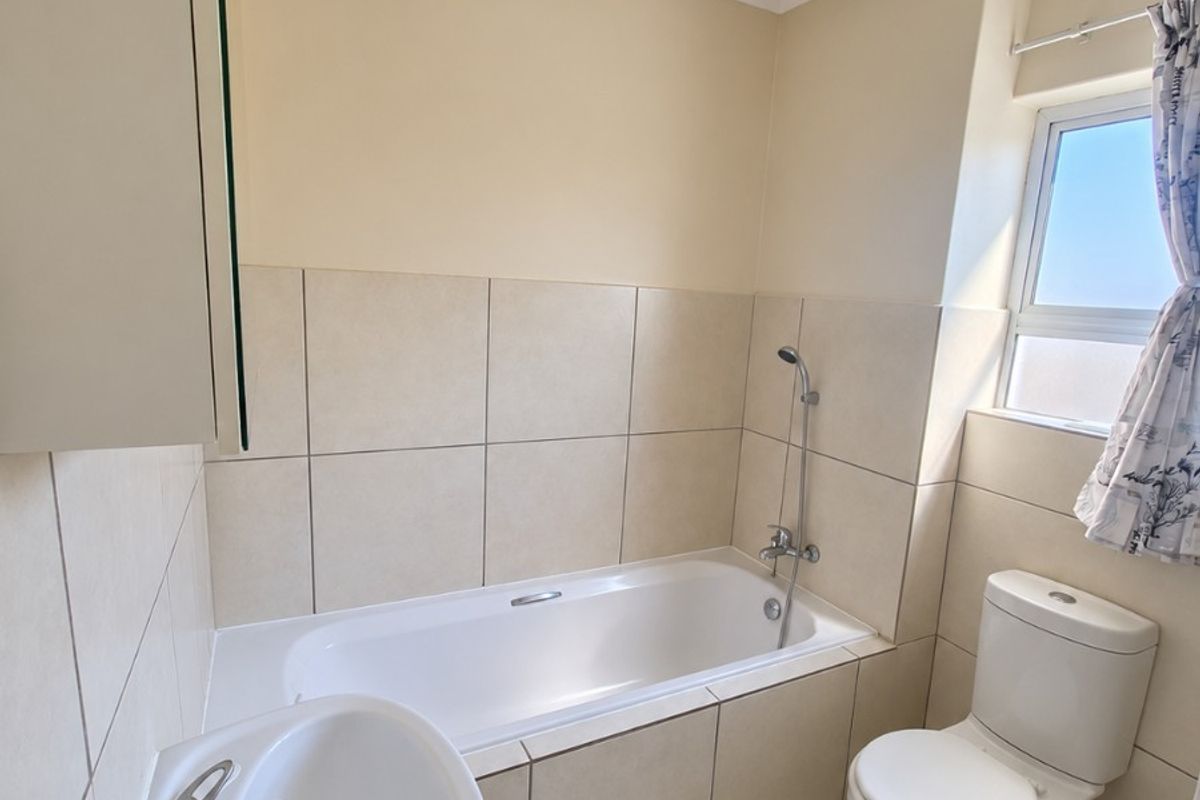 A functional bathroom featuring a bathtub with shower mixer, pedestal basin, and toilet, finished with neutral wall and floor tiles.