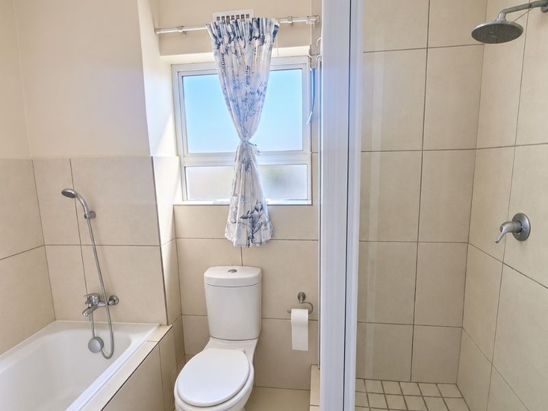 A functional bathroom featuring a separate bathtub and shower enclosure with neutral wall and floor tiling.