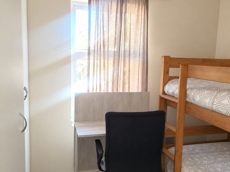A functional bedroom featuring carpeted flooring, a built-in wardrobe, and a window with a curtain rod, providing a practical living space.