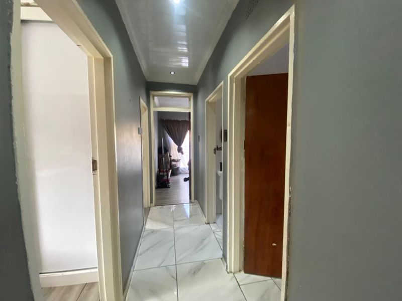 A central hallway featuring white marble-look floor tiles, grey painted walls, and recessed ceiling lighting, providing access to multiple rooms.
