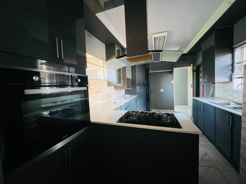 Modern kitchen featuring dark cabinetry, quartz countertops, built-in oven, gas hob, and a stainless steel extractor fan.