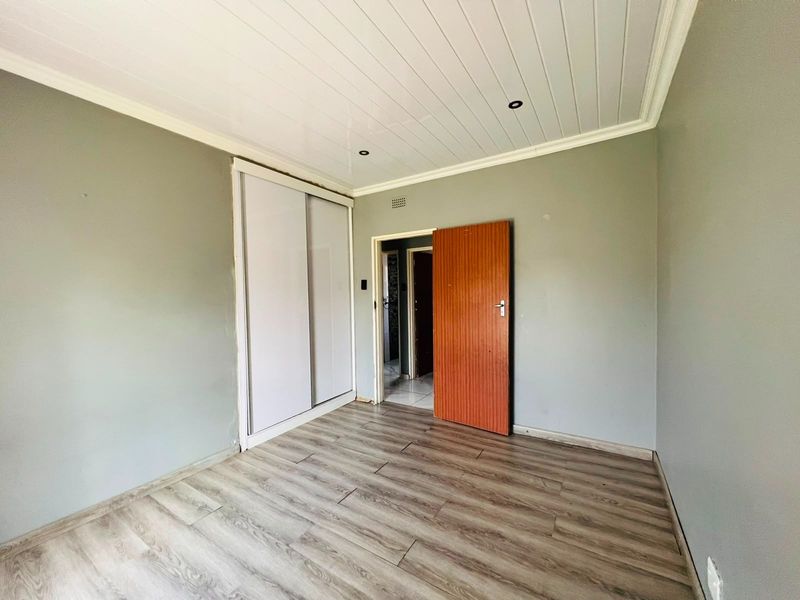 An empty bedroom featuring laminate flooring, built-in sliding door wardrobes, and a modern tongue and groove ceiling with recessed lighting.