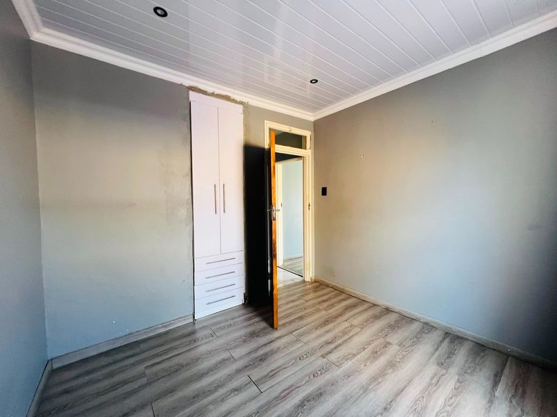 An empty bedroom featuring laminate flooring, a built-in wardrobe, and modern PVC ceiling panels with recessed lighting.