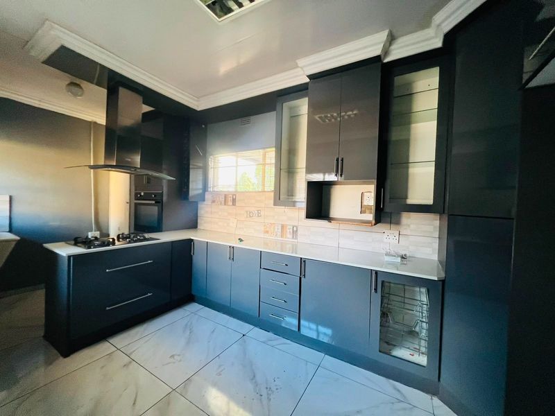 Modern kitchen featuring sleek dark cabinetry, stone countertops, integrated gas hob, extractor fan, and high-quality tiled flooring.