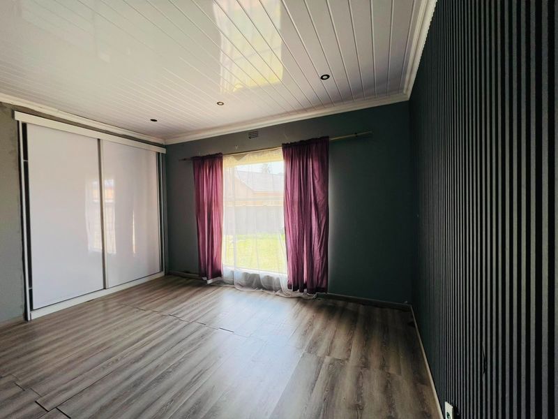 Spacious bedroom featuring modern laminate flooring, a built-in sliding wardrobe, a decorative slatted feature wall, and a clean tongue and groove ceiling.