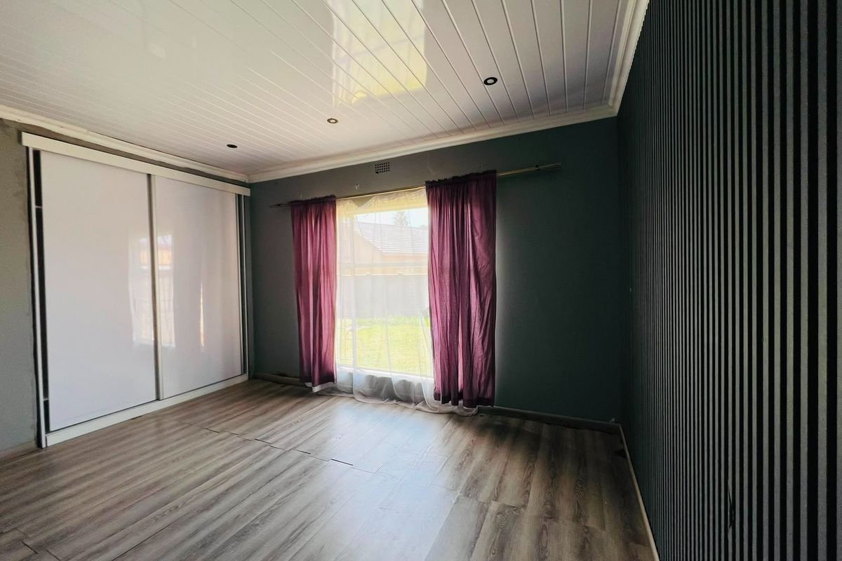 Spacious bedroom featuring modern laminate flooring, a built-in sliding wardrobe, a decorative slatted feature wall, and a clean tongue and groove ceiling.