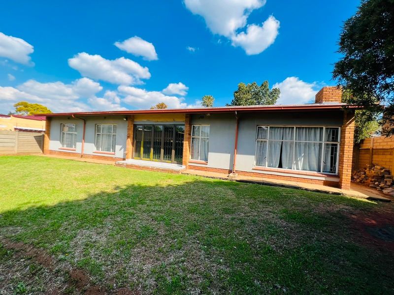 Rear view of the house featuring a brick chimney, sliding glass doors, and a spacious backyard with a perimeter brick boundary wall.
