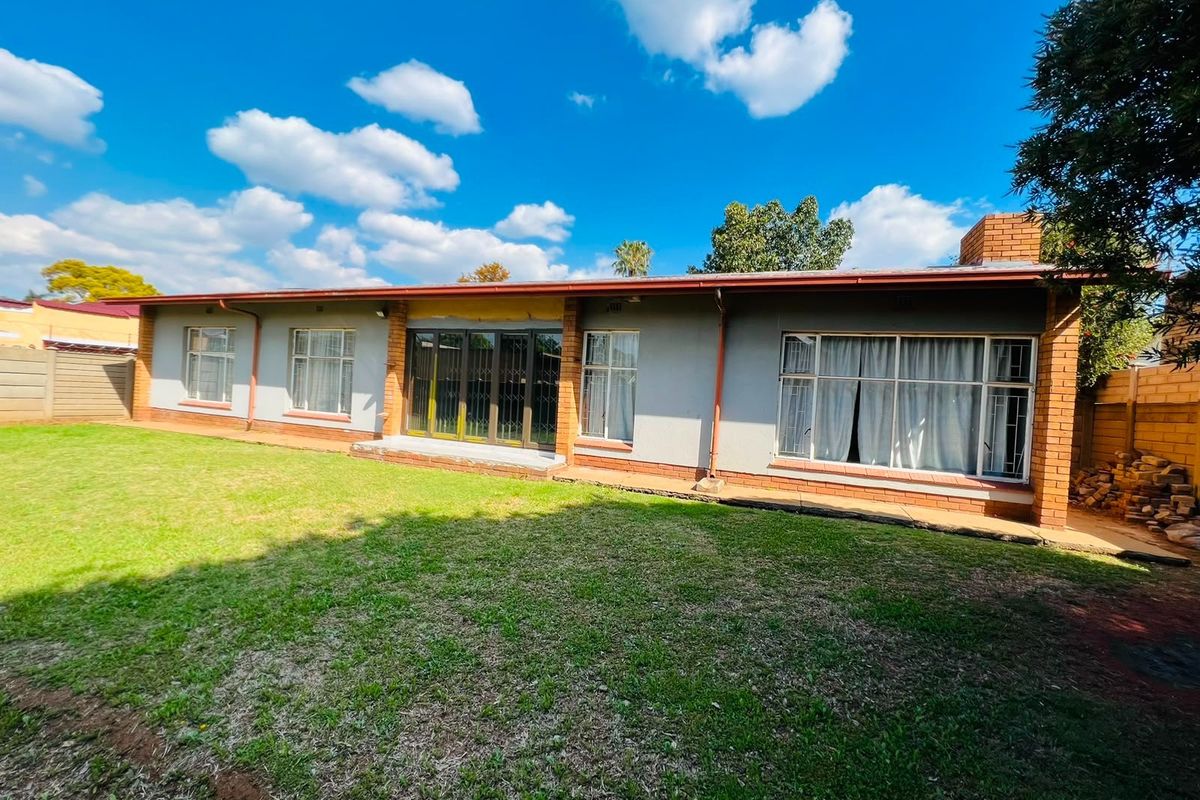 Rear view of the house featuring a brick chimney, sliding glass doors, and a spacious backyard with a perimeter brick boundary wall.