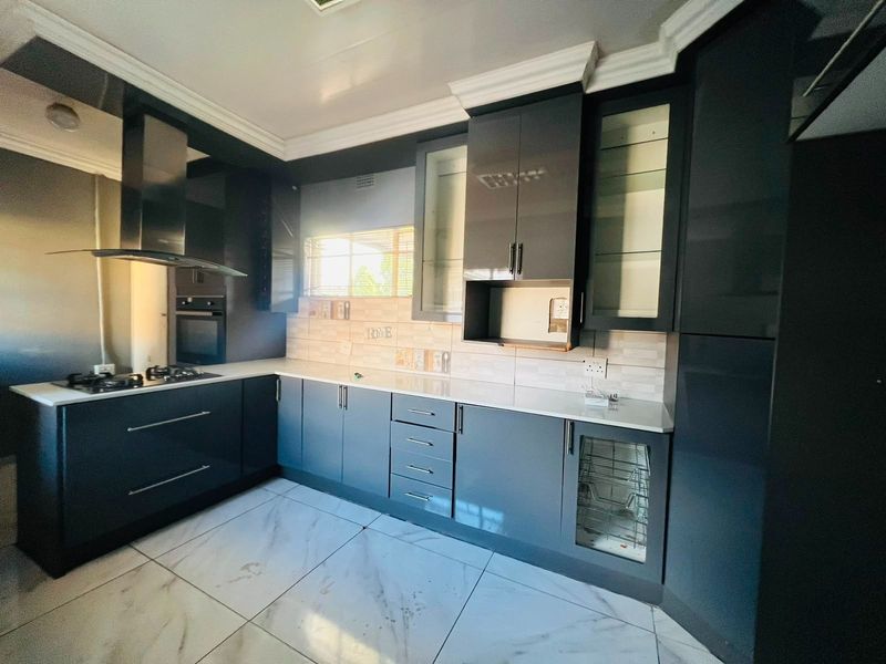 Modern kitchen featuring dark grey cabinetry, stone countertops, built-in oven, gas hob, extractor fan, and polished porcelain floor tiles.