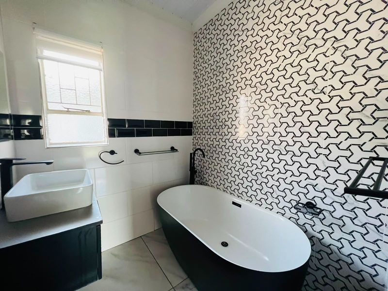Modern bathroom featuring a freestanding bathtub, vessel sink, vanity cabinet, and a striking geometric tiled feature wall with contemporary black matte fixtures.