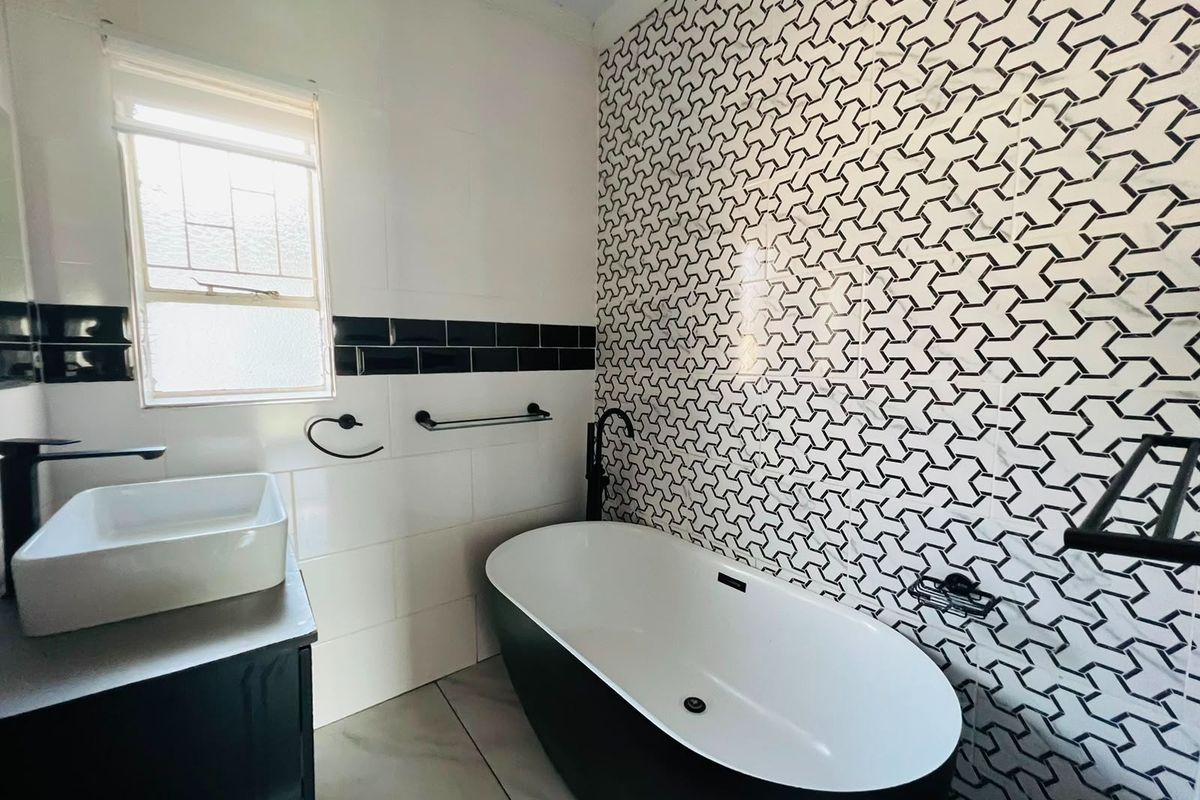 Modern bathroom featuring a freestanding bathtub, vessel sink, vanity cabinet, and a striking geometric tiled feature wall with contemporary black matte fixtures.