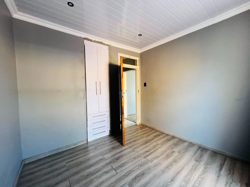 An empty bedroom featuring laminate flooring, a built-in wardrobe, and a white tongue and groove ceiling with recessed lighting.