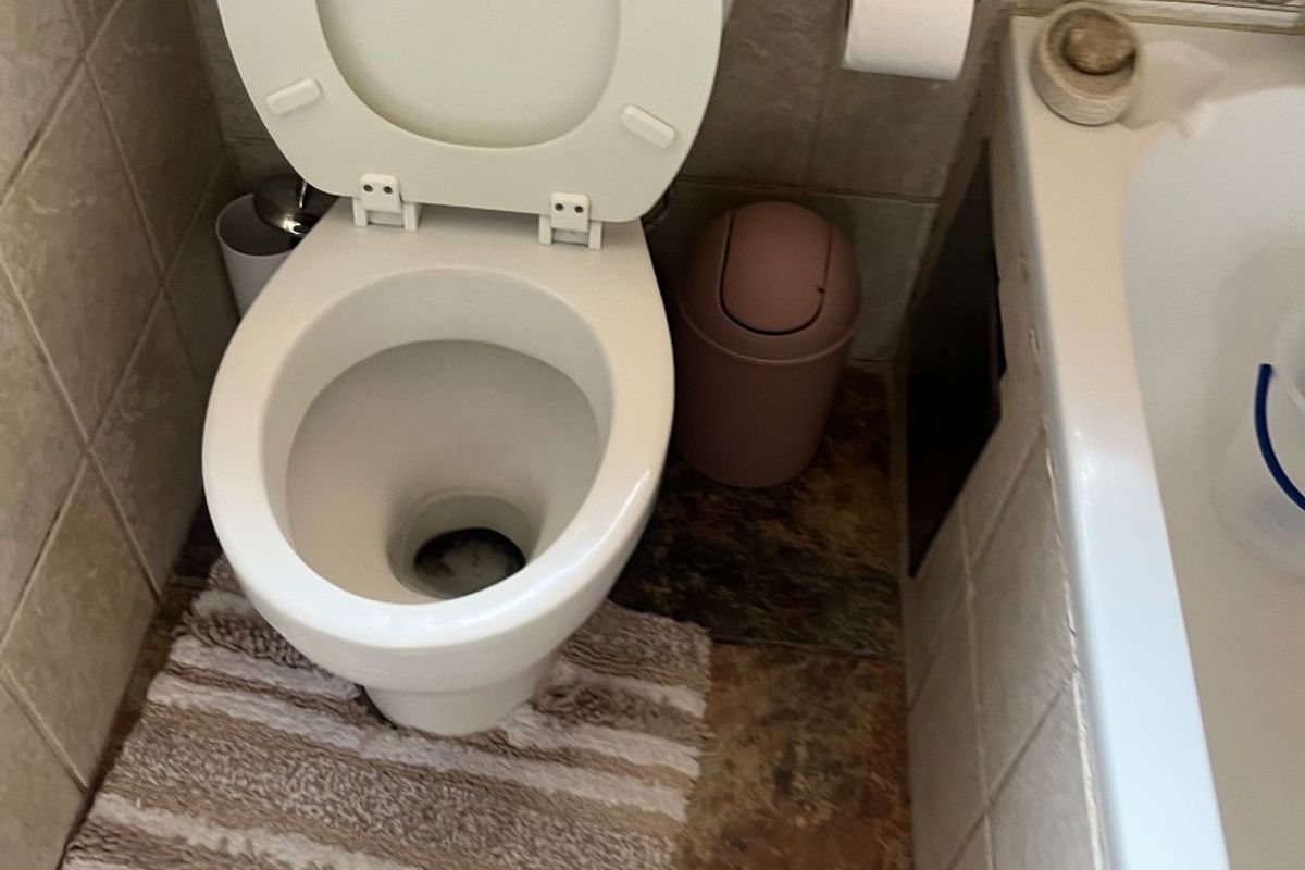 A compact bathroom featuring a standard toilet and bathtub with tiled finishes, currently showing visible damage to the wall tiling.