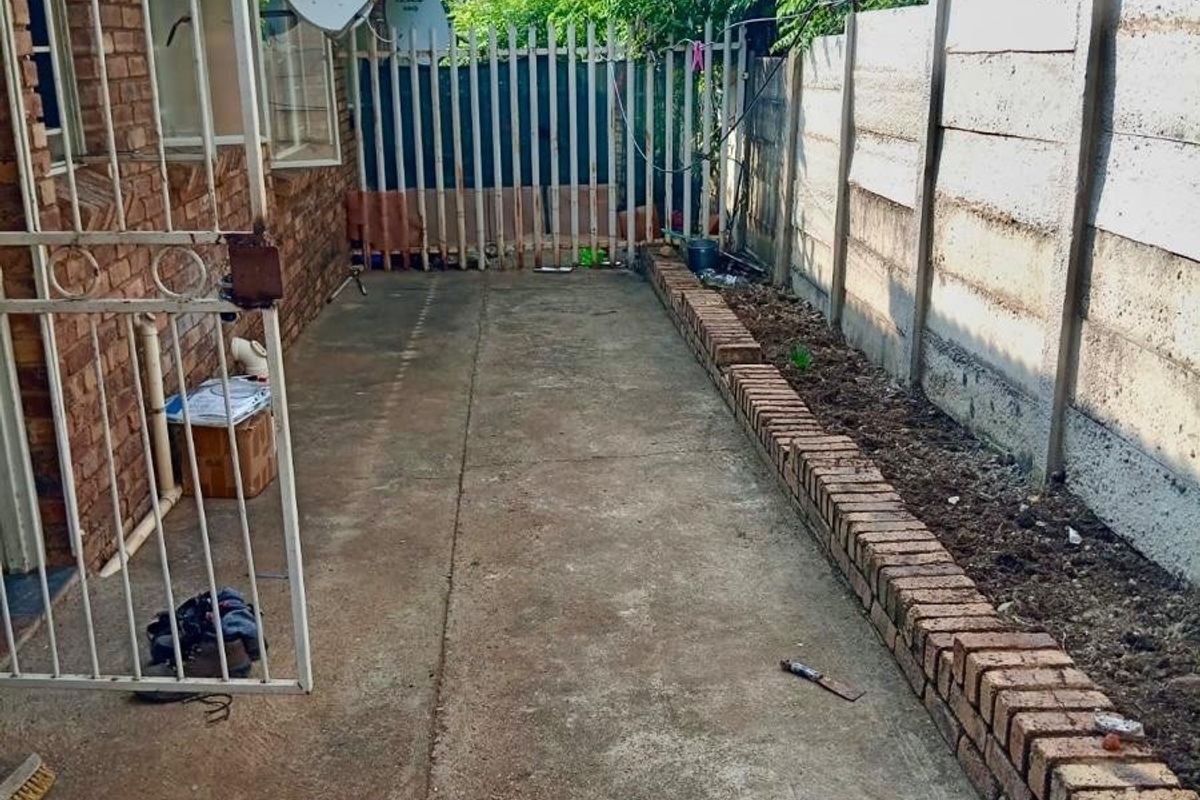 A narrow rear exterior area featuring concrete paving, a brick boundary edge, and a secure perimeter wall with razor wire.