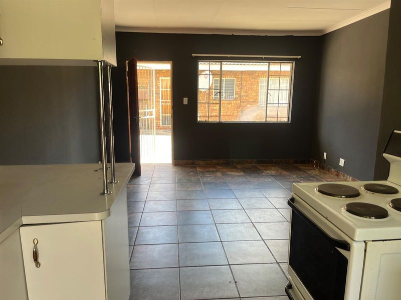 Open-plan living and kitchen area featuring tiled flooring, dark painted walls, and direct access to an exterior courtyard through a security gate.