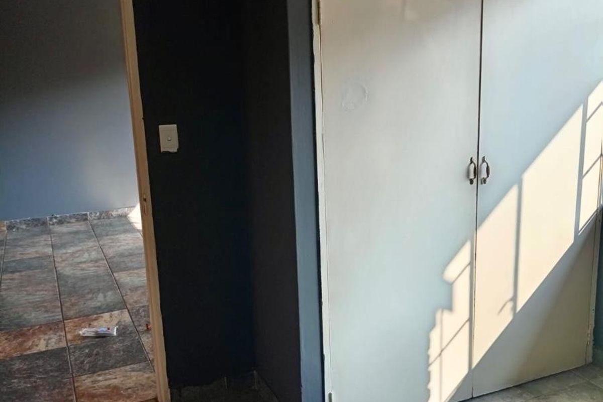 An empty bedroom featuring built-in cupboards and tiled flooring, with a doorway leading to an adjacent room.