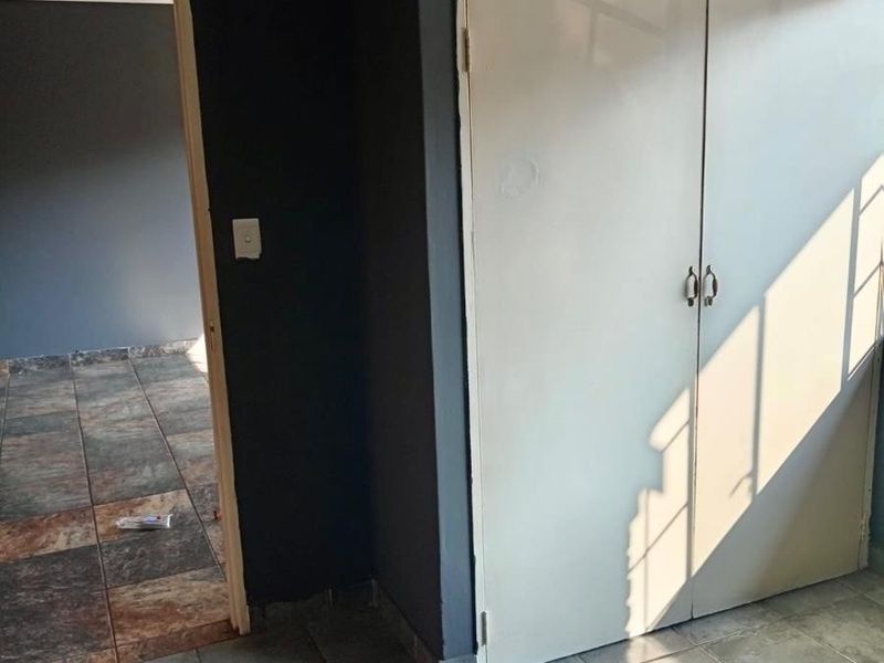 An empty bedroom featuring built-in cupboards and tiled flooring, with a doorway leading to an adjacent room.