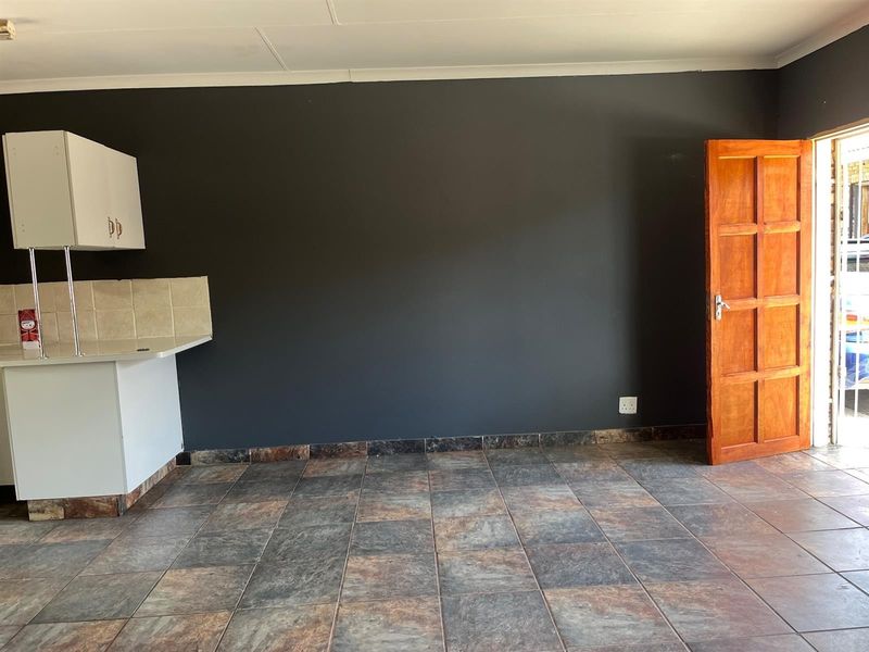 An open-plan living area featuring dark accent walls, tiled flooring, and a partial kitchen setup with built-in cabinetry and a tiled backsplash.
