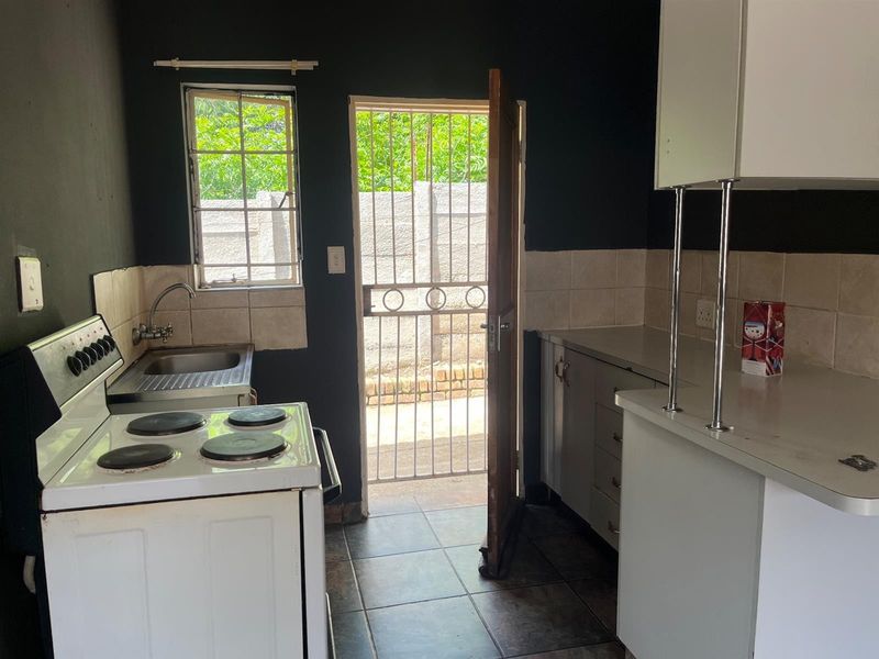 A functional kitchen featuring built-in cabinetry, laminate countertops, a stainless steel sink, and direct access to an outdoor area via a security gate.